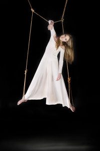 Young woman gymnast in white dress on rope on black background